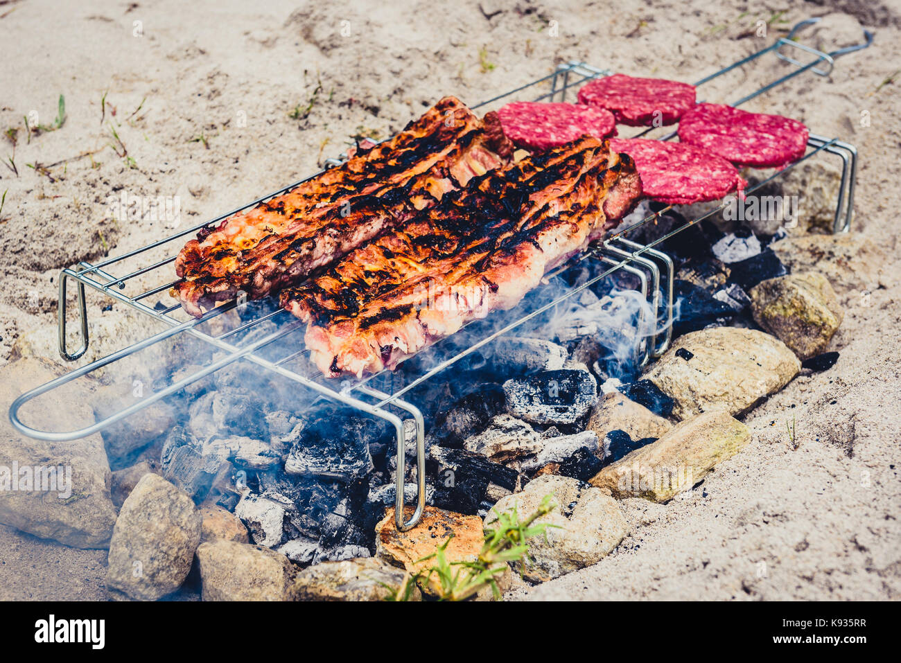 Pork ribs and burgers on homemade improvised BBQ barbecue grill. Making  Churrasco and burgers on coal, fire, briquettes BBQ grill in the sand with  roc Stock Photo - Alamy