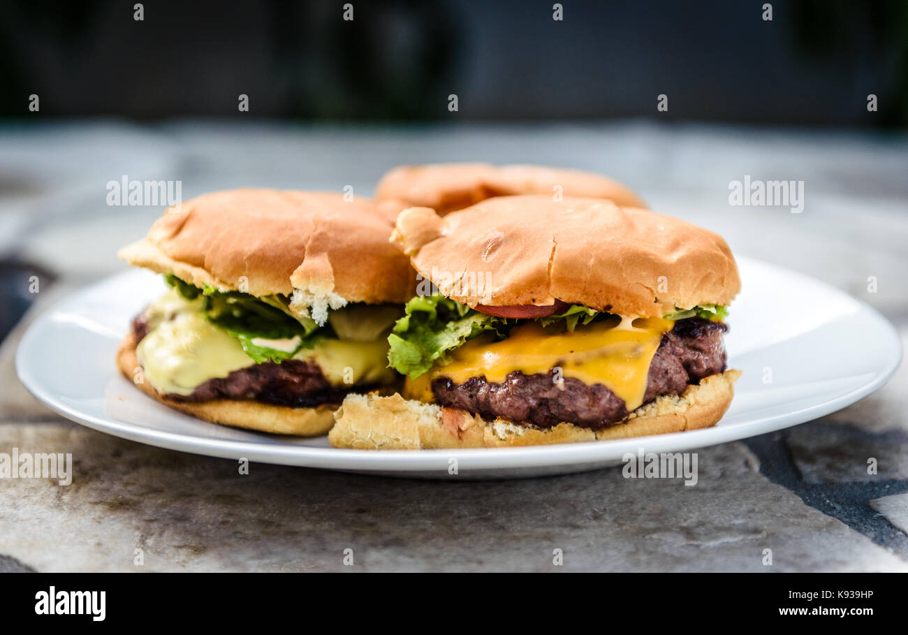 Home made burgers on a plate on stone paved terrace. Delicious home coked hand made craft burgers on a stone table. Stock Photo