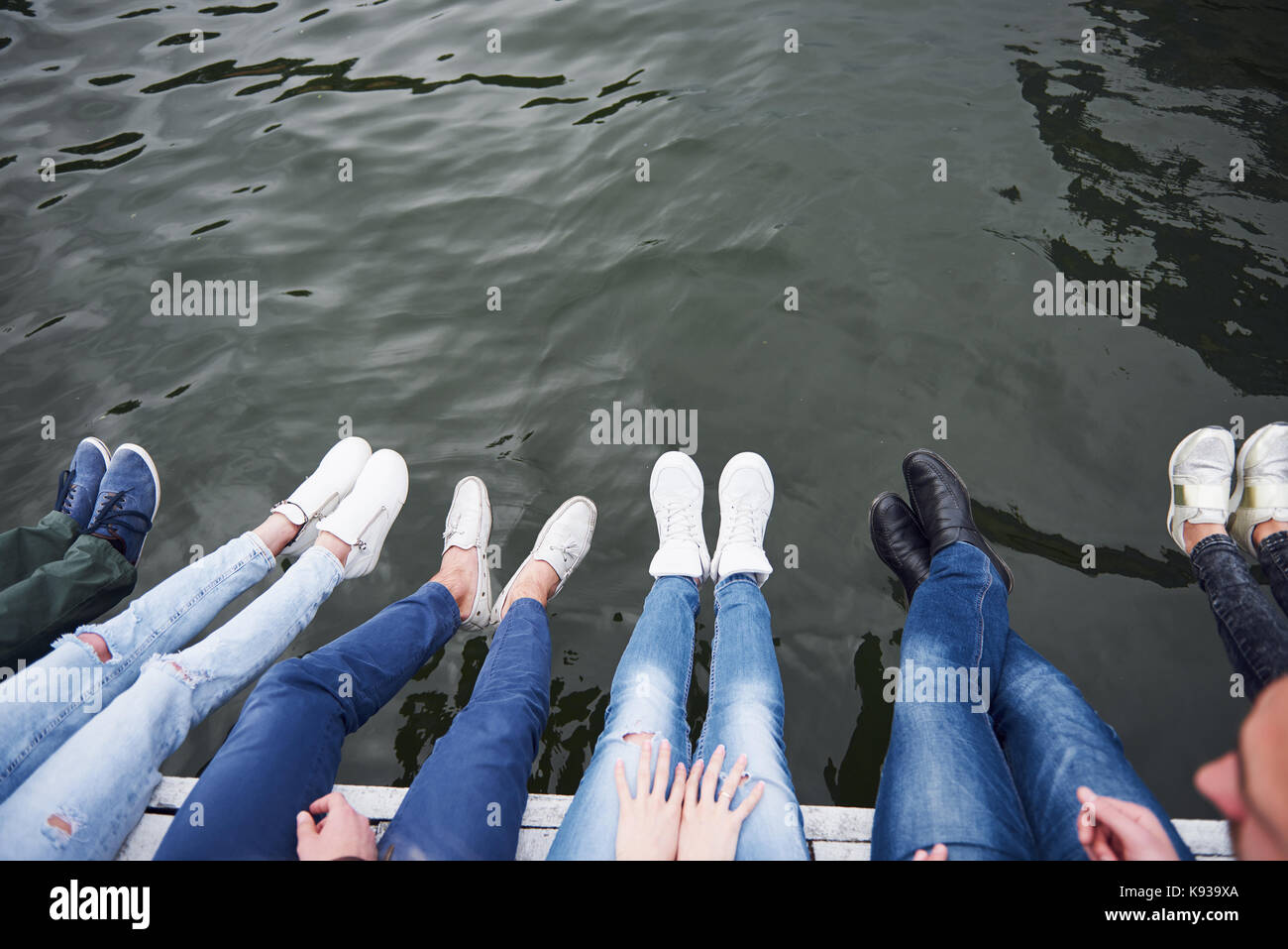 Young people friends sitting on the river bridge, lifestyle, feet over blue water Stock Photo
