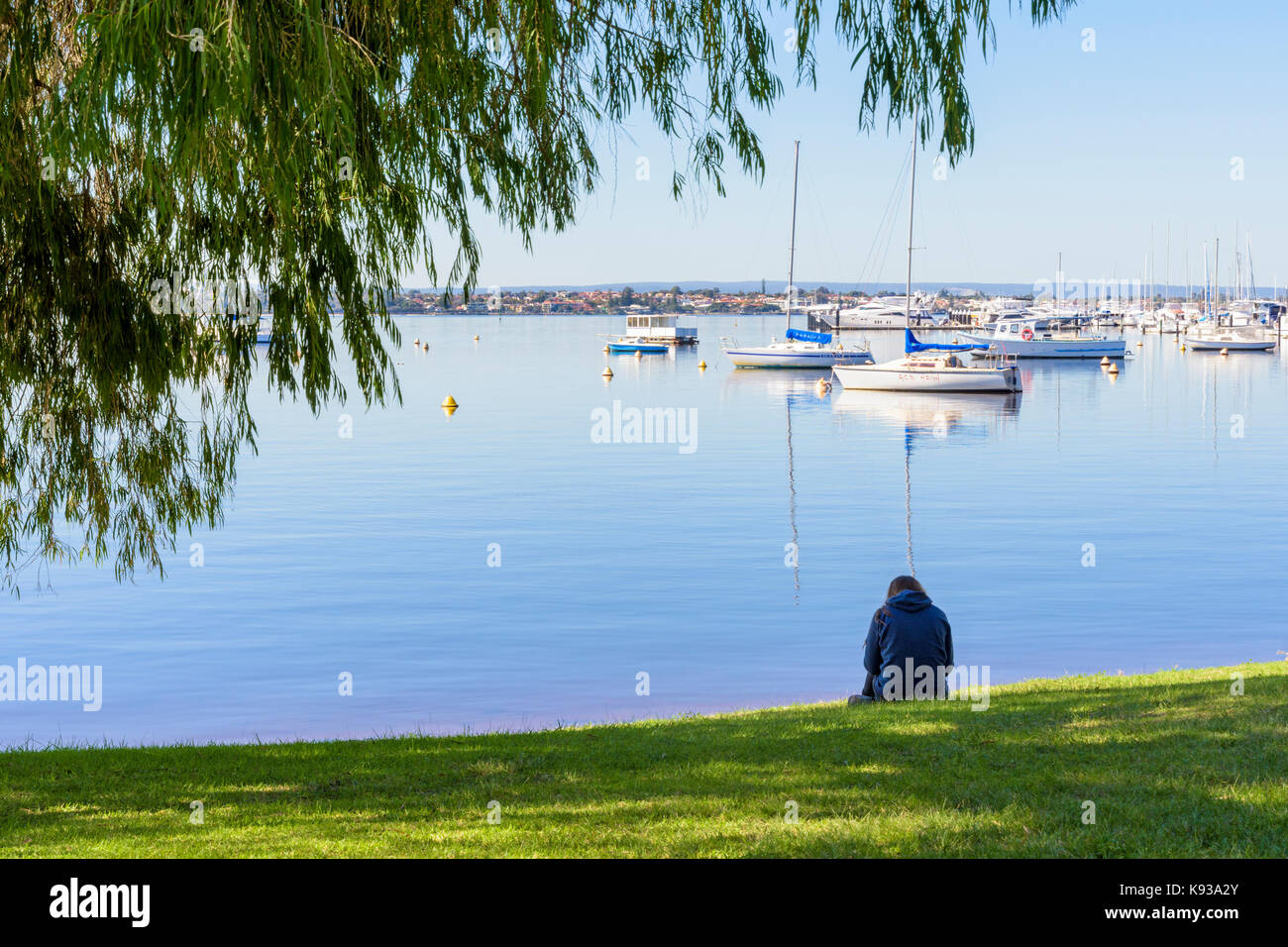 Lone student sits on the foreshore of Matilda Bay on the Swan River near the University of Western Australia, Crawley, Perth, Western Australia Stock Photo