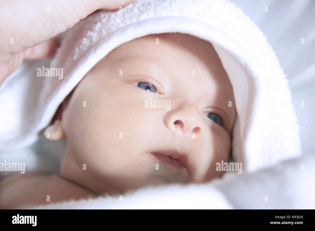 Close-up portrait of a very young newborn toddler wrapped in fresh white baby clothes. Stock Photo