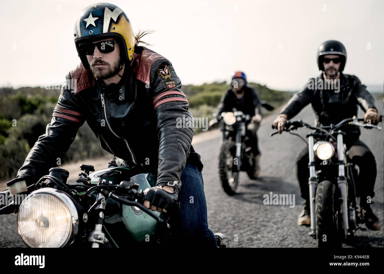 Three men wearing open face crash helmets and sunglasses riding cafe racer  motorcycles along rural road Stock Photo - Alamy