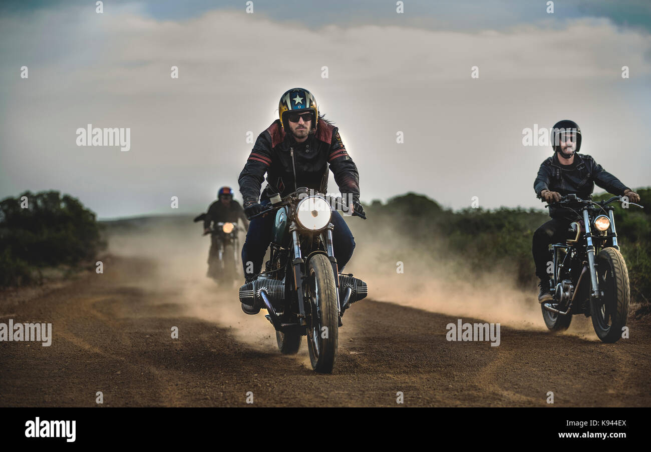 Three men riding cafe racer motorcycles along dusty dirt road Stock ...