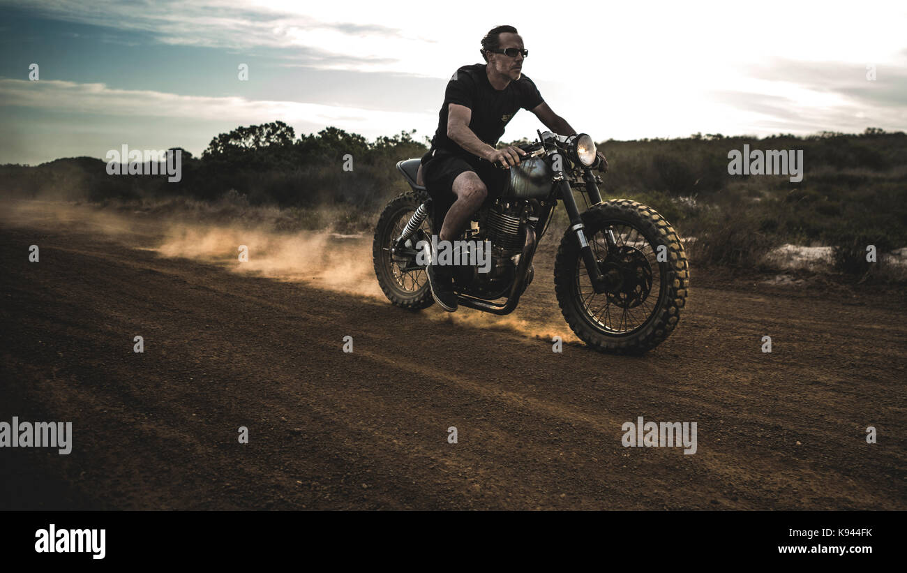 Man wearing shorts and sunglasses riding cafe racer motorcycle on a
