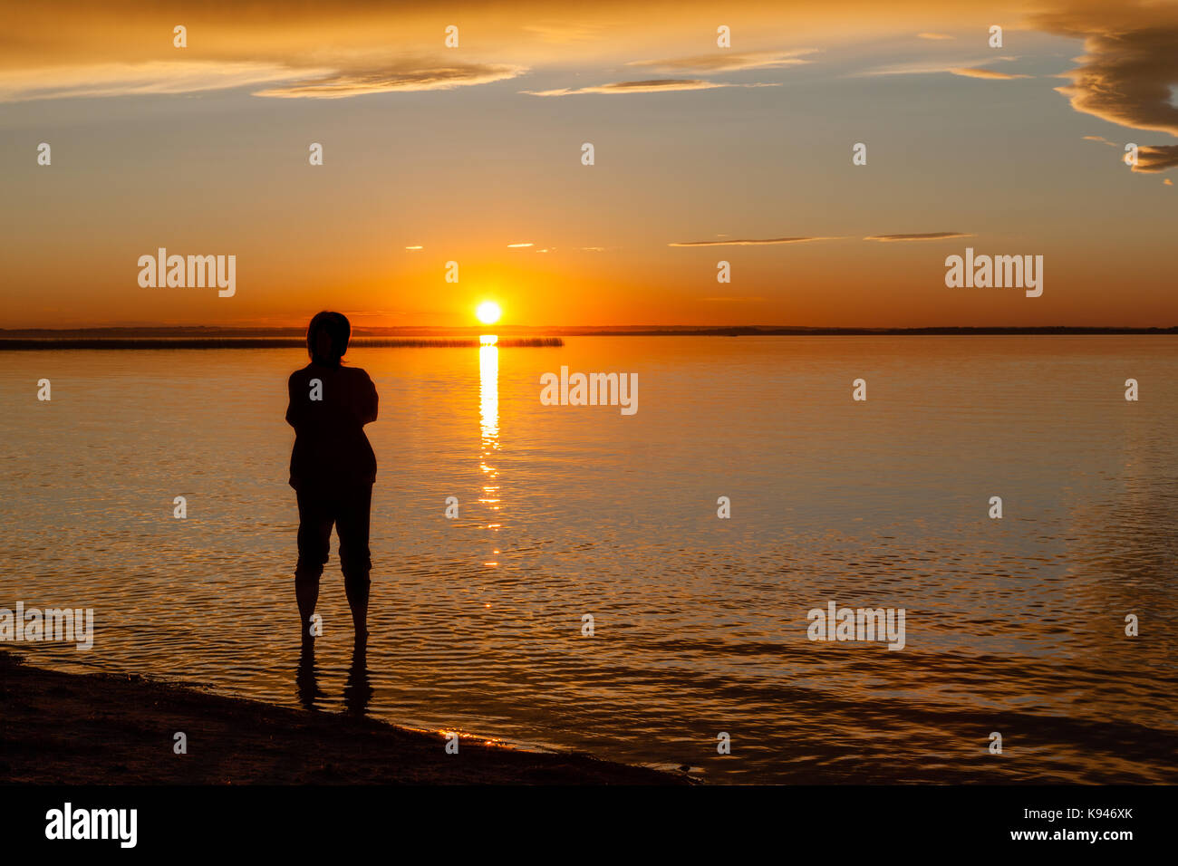 Silhouette of a woman on the beach water's edge watching sunset ...