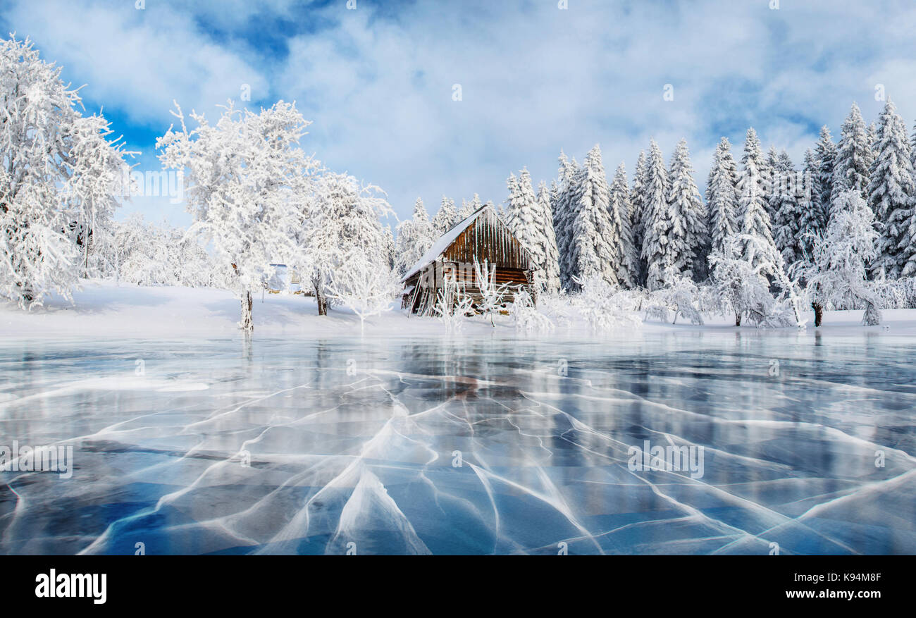 Blue ice and cracks on the surface of the ice. Frozen lake under a blue sky in the winter. Cabin in the mountains. Mysterious fog. Carpathians. Ukraine, Europe Stock Photo