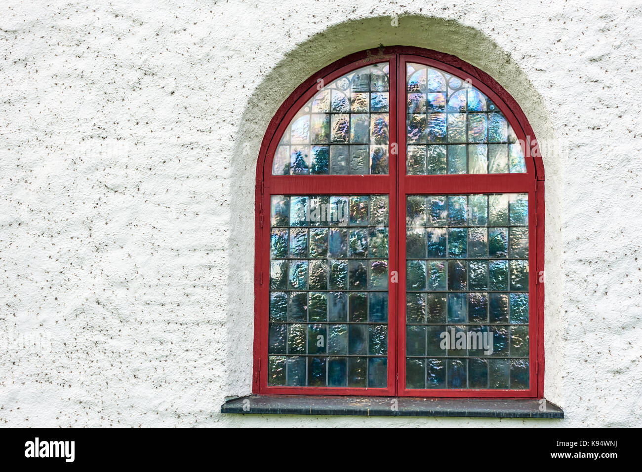 Iridescent window with red frame on white church. Stock Photo