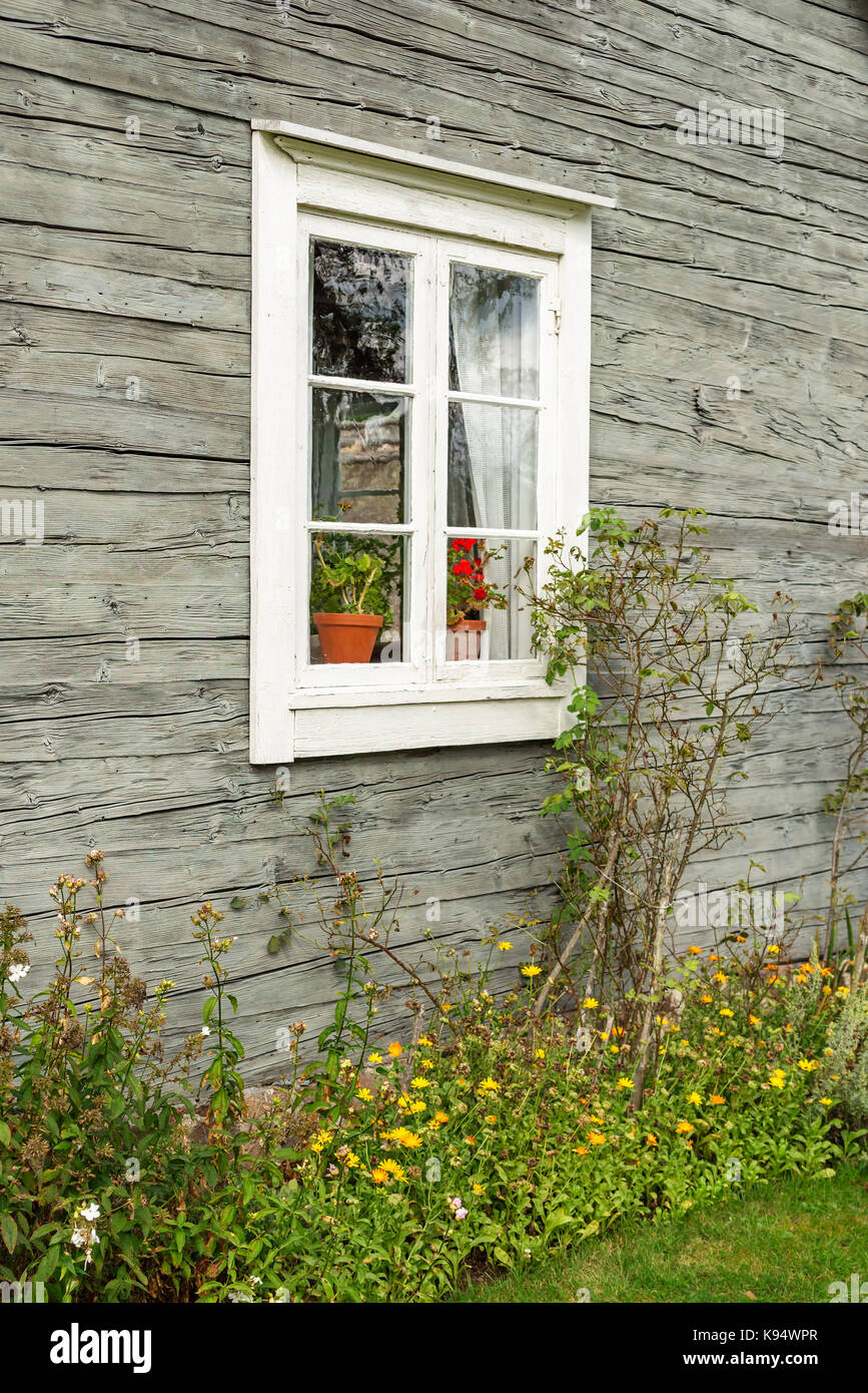 Glass window on old cabin with flowerbed underneath. Stock Photo