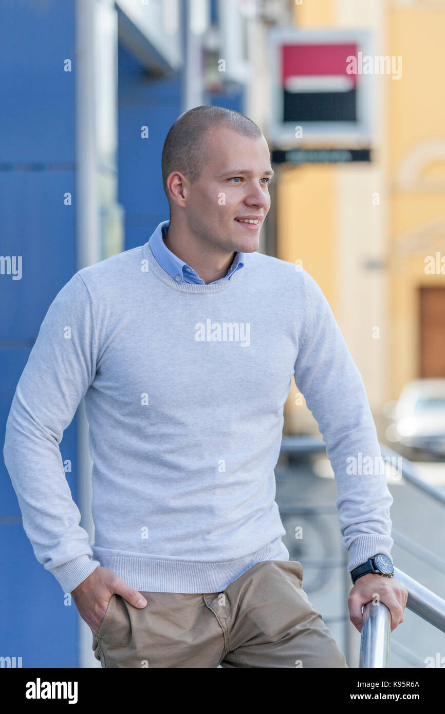 Handsome and attractive young man in a shirt  leaning against the metal fence and waiting for someone. Portrait of an urban  and smiling young man out Stock Photo