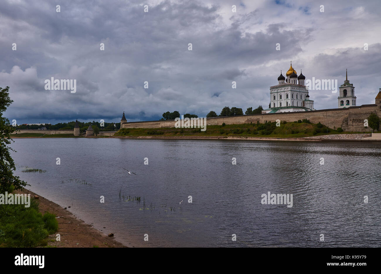 Summer, evening. The sky is covered with clouds. A gull flies over the river. On the opposite bank is the Pskov Kremlin.Russia, Pskov region,landscape Stock Photo