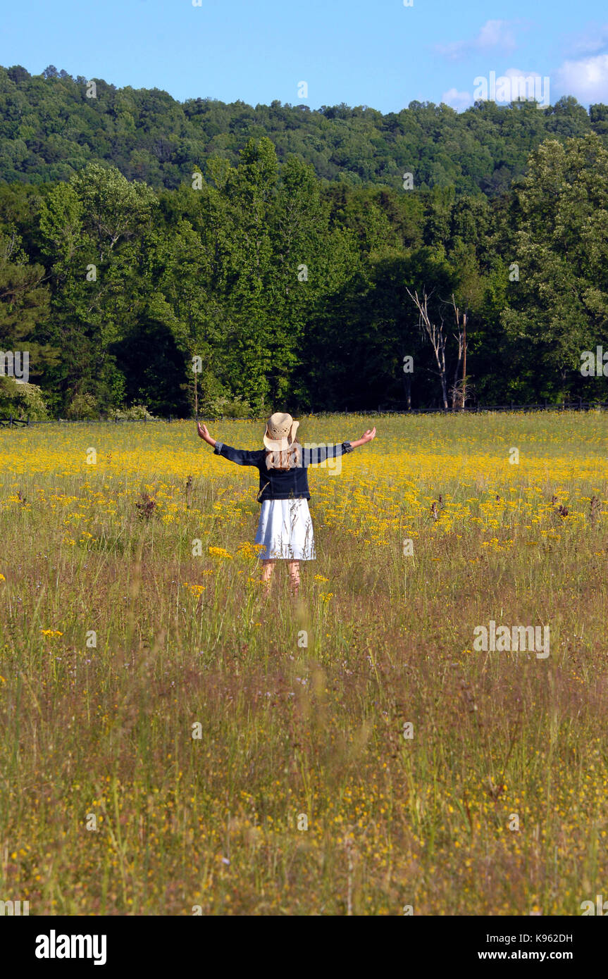 Young girl stands in the middle of a field of yellow flowers. Her arms ...