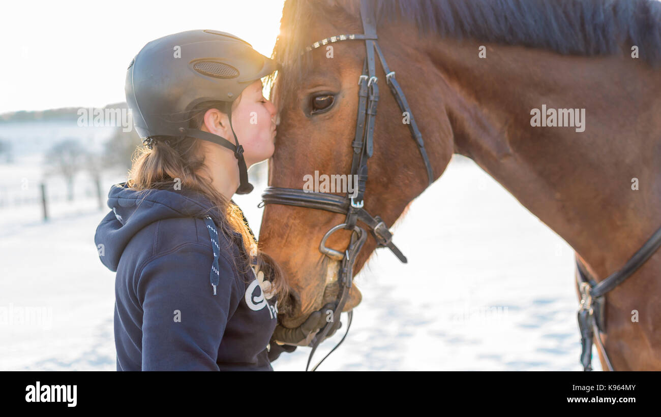 Woman rider kisses Hanoverian horse in front of snowy scenery Stock Photo