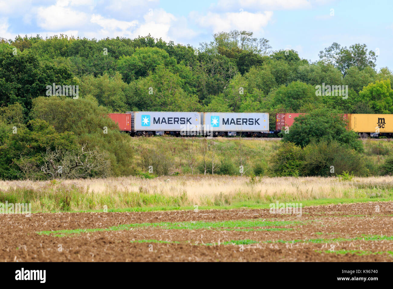 Shipping containers being transported by rail though the British countryside. Stock Photo