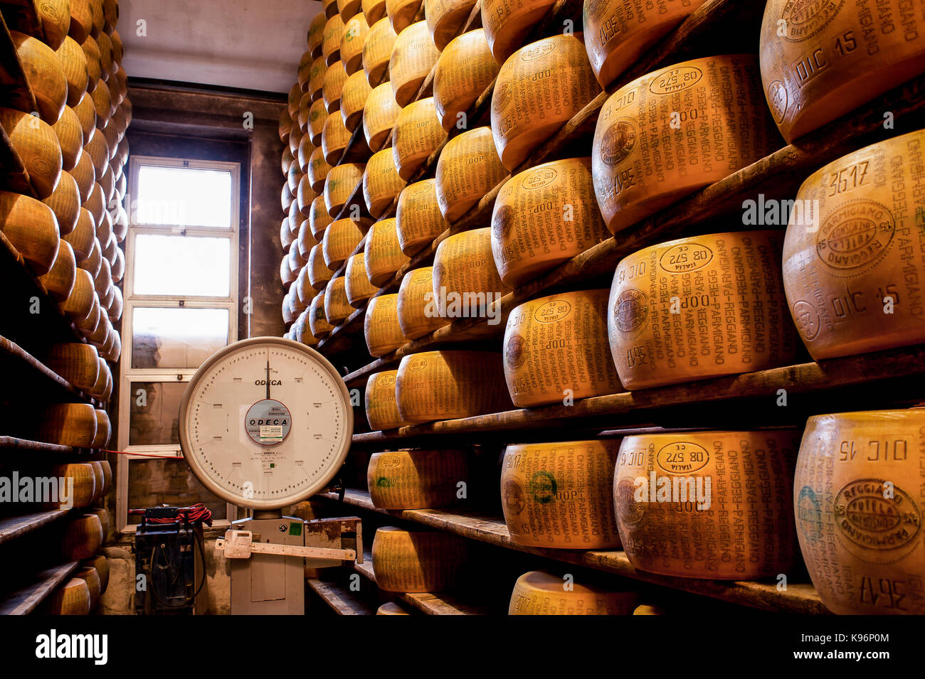 Whole Parmigiano-Reggiano cheeses sit on storage racks during the aging process next to big balance to weight them Stock Photo