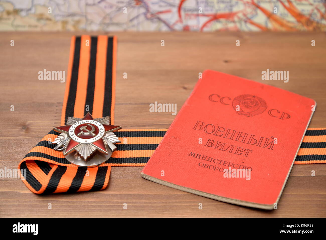 Order of the Patriotic War in St. George bow and Soviet military ID lie on a wooden table against the background of military maps Stock Photo