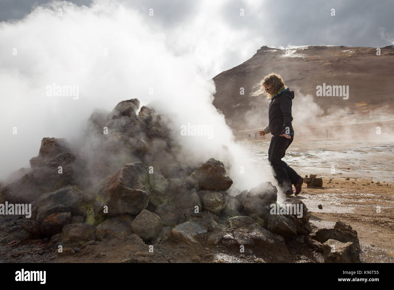 A woman walks among the steaming mud pots geothermal area near Lake Myvatn. Stock Photo