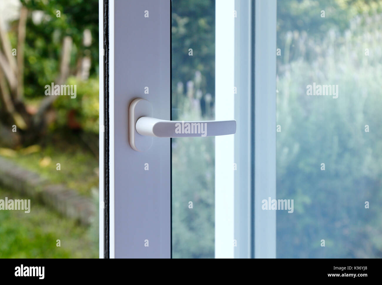 Open door of a family home. Close-up of the lock on the sliding door with the yard of background. White PVC door and double glass. Stock Photo