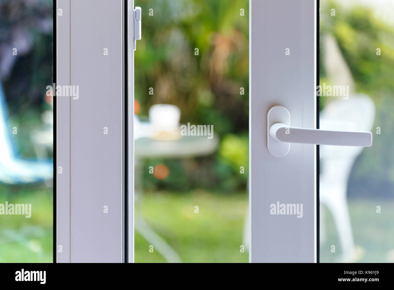 Open door of a family home. Close-up of the lock on the sliding door with the yard of background. White PVC door and double glass. Stock Photo