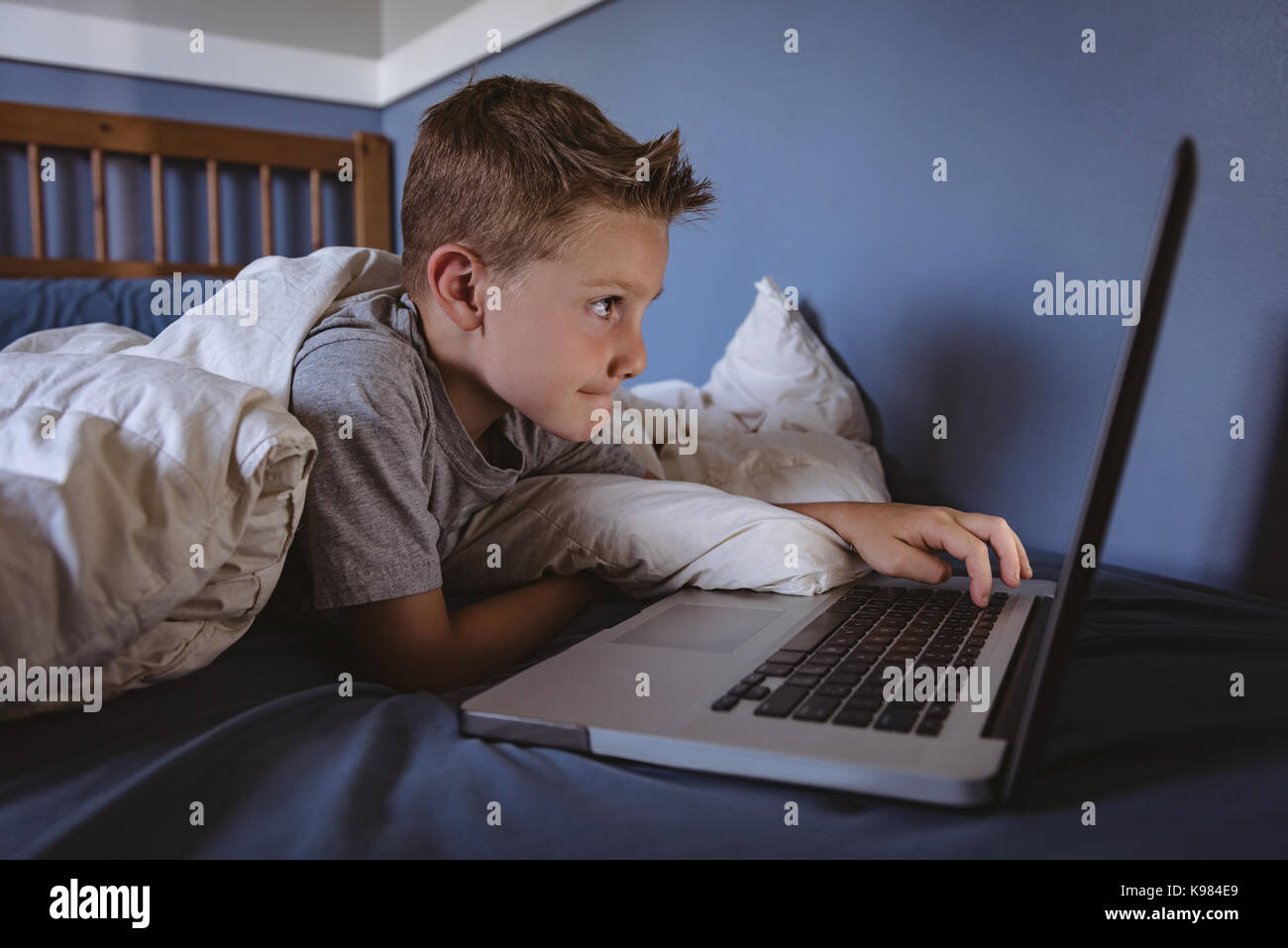 Cute boy using laptop in bedroom Stock Photo - Alamy