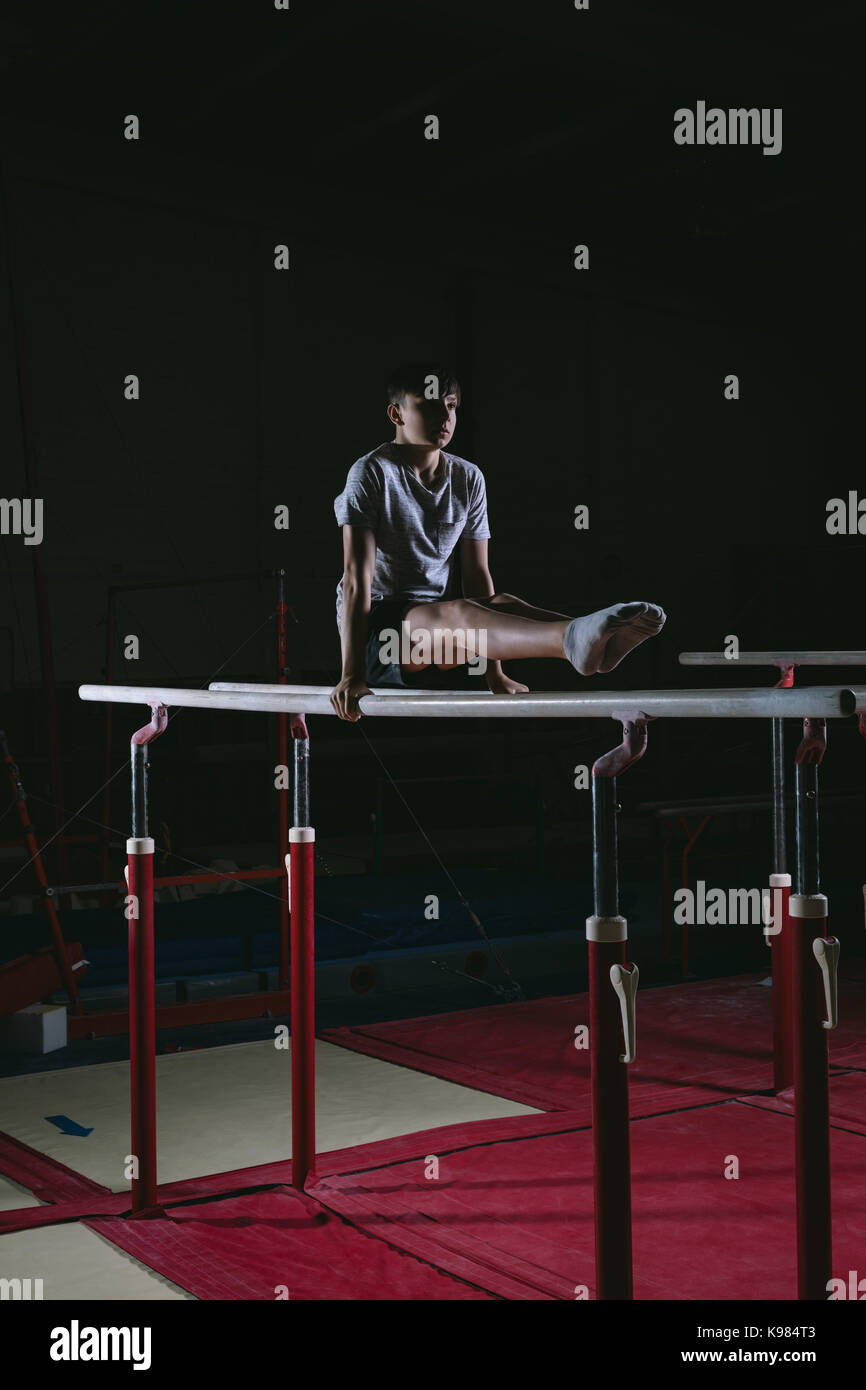 Male gymnast practicing gymnastics on the horizontal bar against black