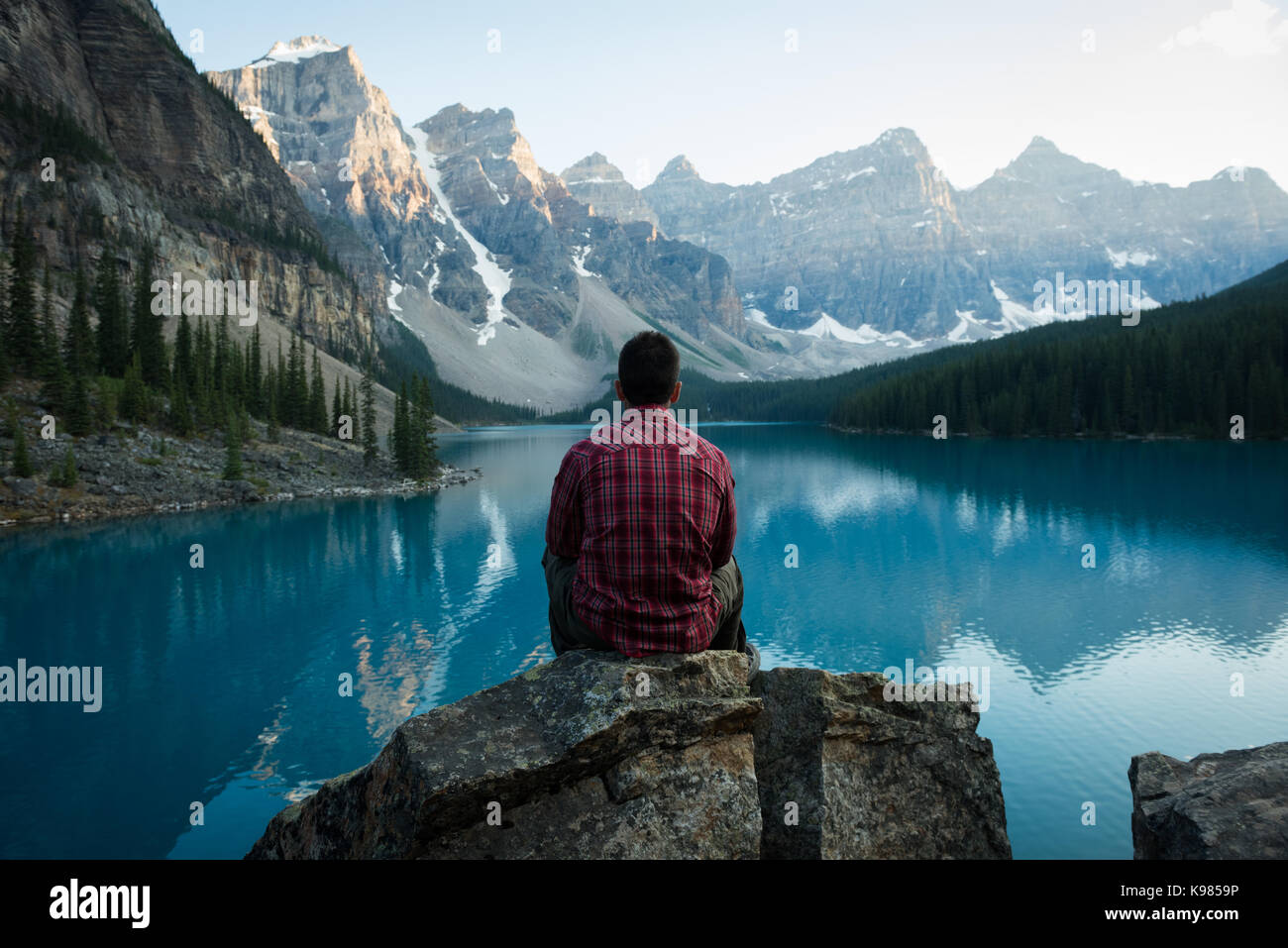 Rear view of man sitting near lake side on a sunny day Stock Photo