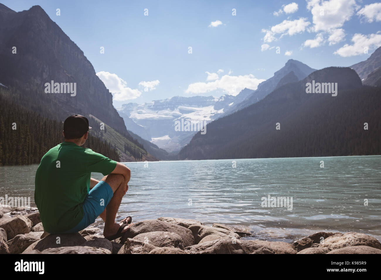 Rear view of man sitting at near lake side on a sunny day Stock Photo