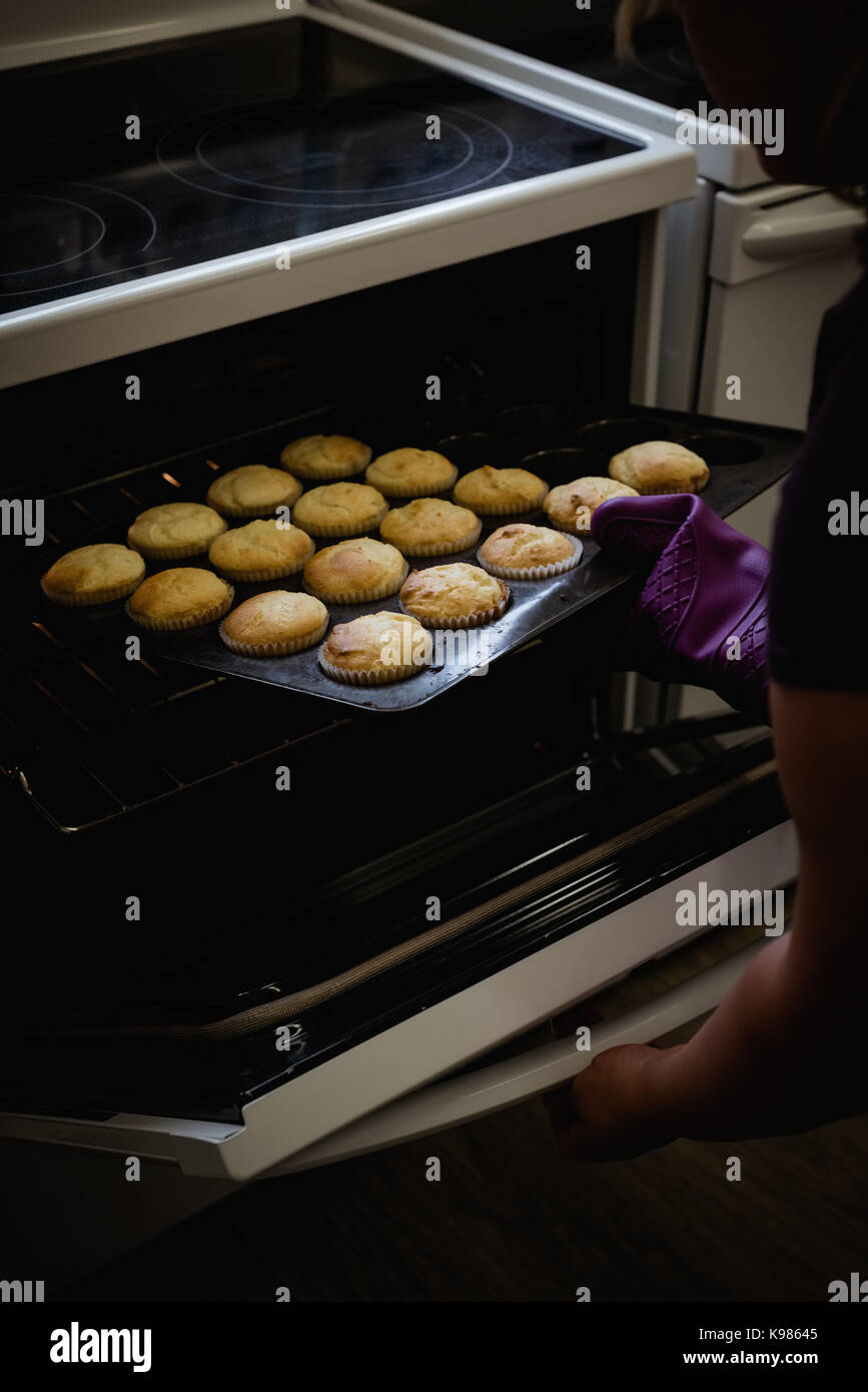 Woman remove freshly baked cupcake from oven in the kitchen Stock Photo