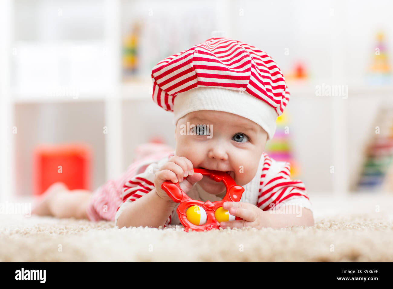 Child girl weared costue biting a toy lying on a carpet at home Stock Photo