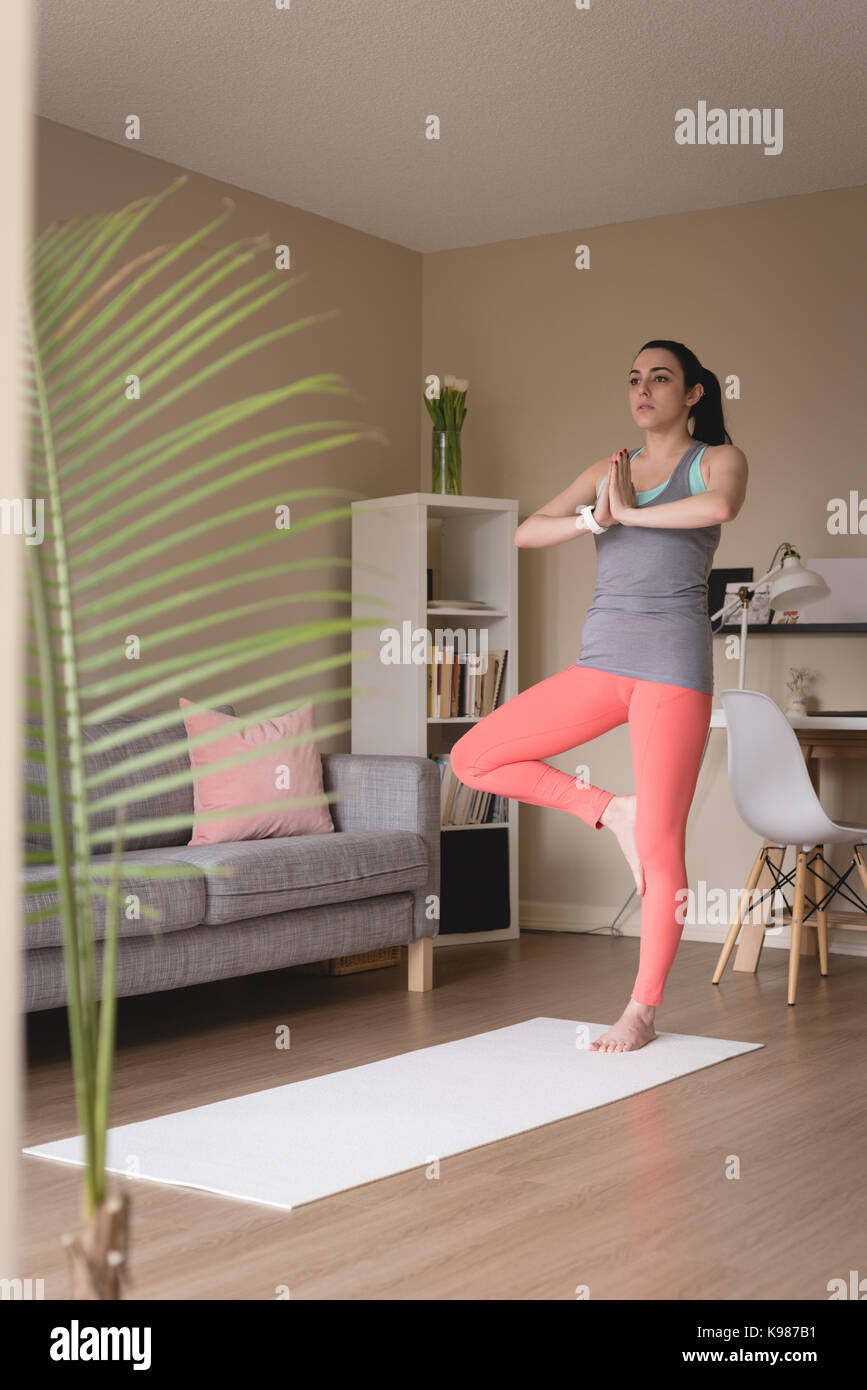 Full length of young woman doing tree pose yoga at home Stock Photo - Alamy