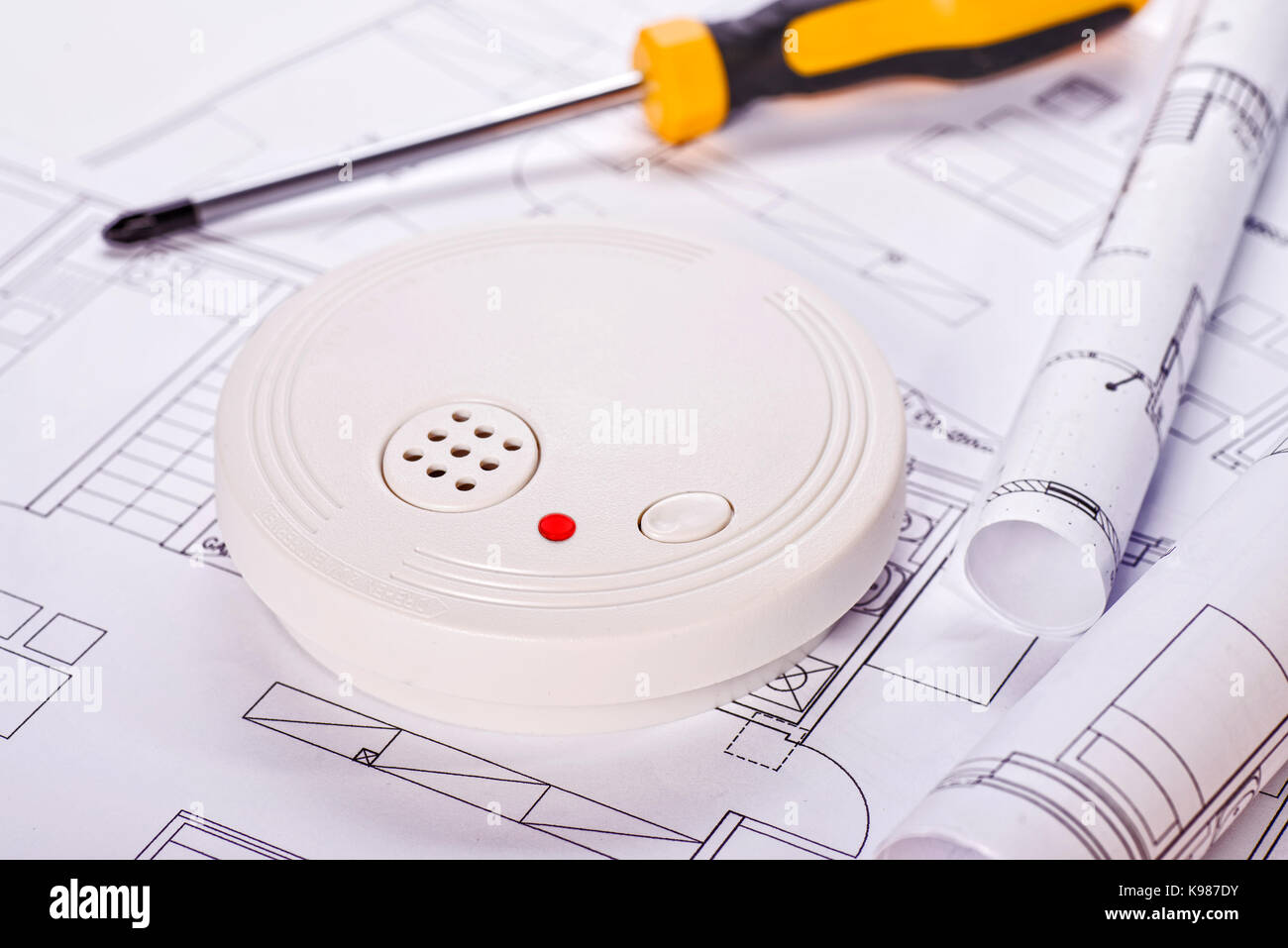 Smoke detector lying on blueprints with screwdriver in the background Stock Photo