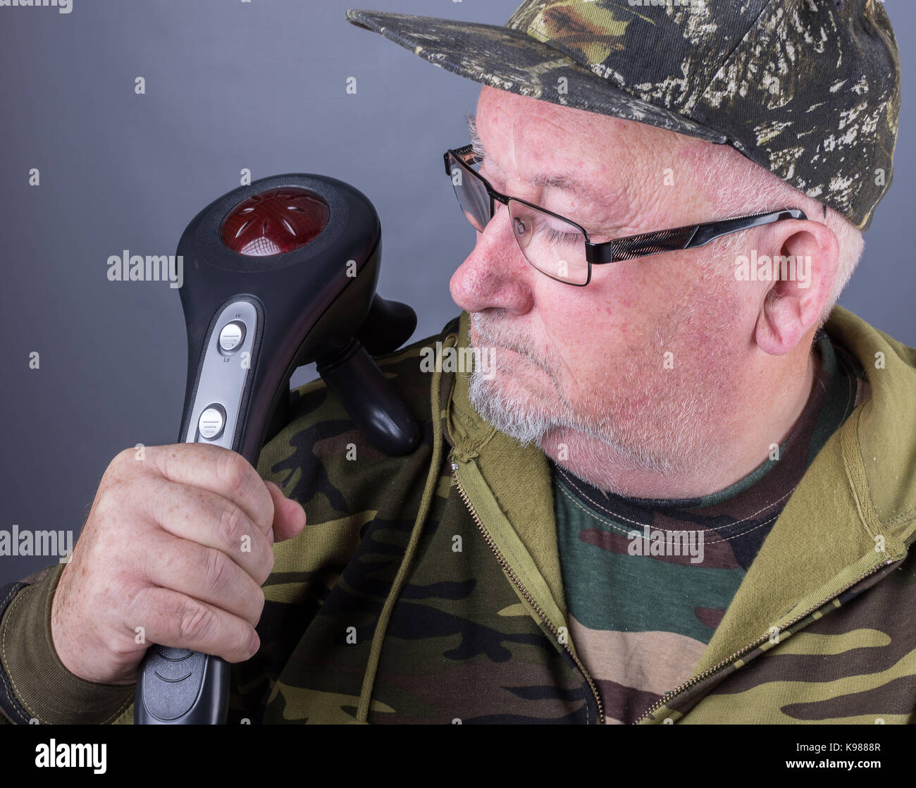 senior elderly man with an electric infrared massager on his shoulder. ir massager providing heat and treatment to shoulder Stock Photo
