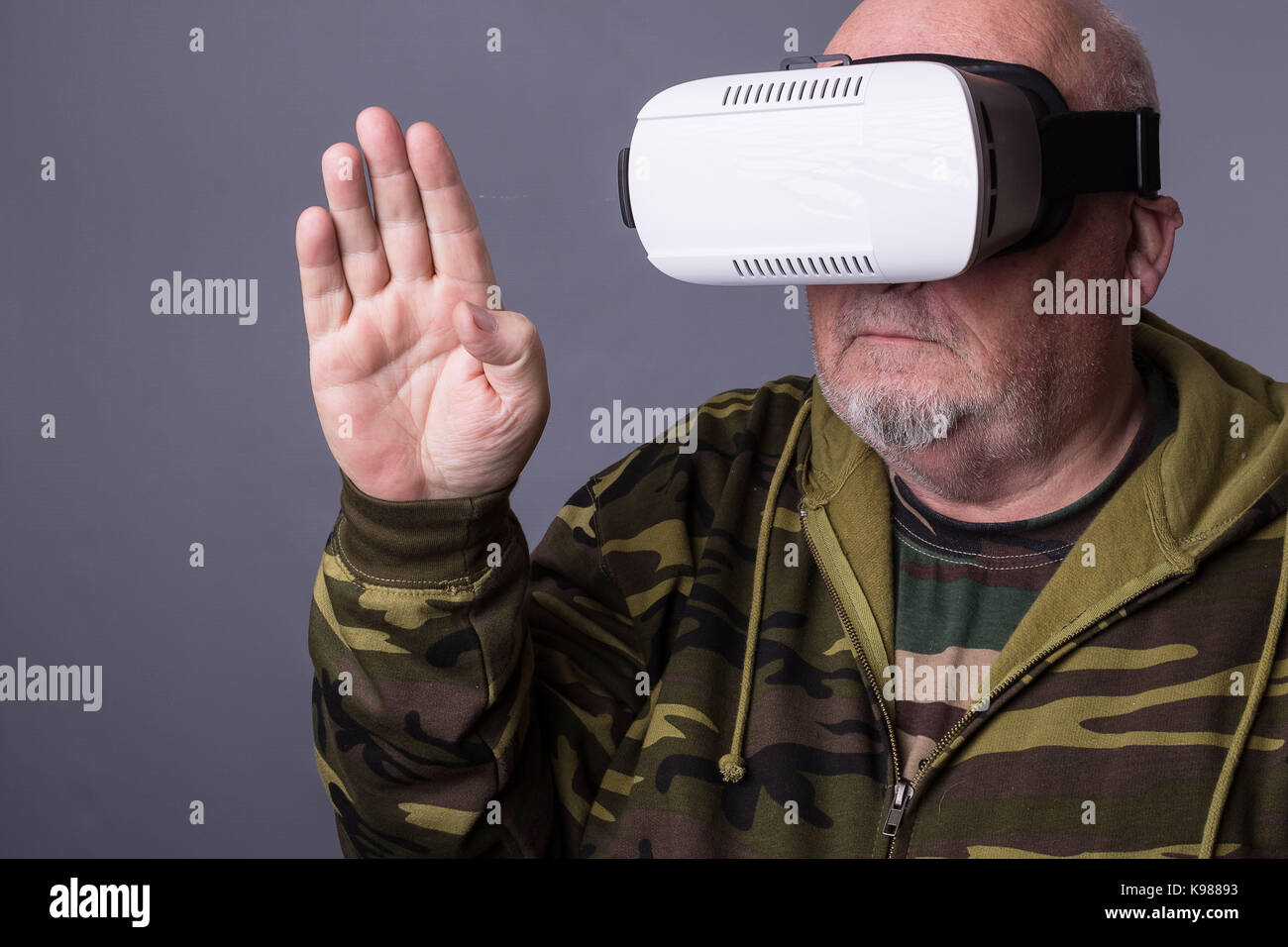 Senior man in wearable technology VR glasses. Confident old man wearing camouflage clothing in virtual reality headset with Interface selective focus  Stock Photo