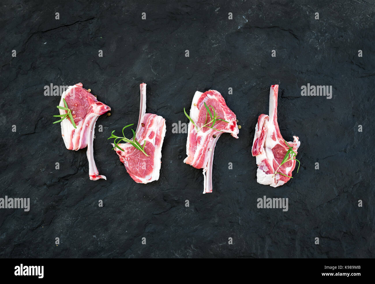 Raw lamb chops. Rack of Lamb with rosemary and spices over black slate