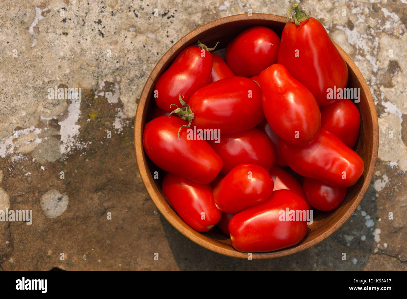 Wooden bowl with fresh picked organic roma tomatoes on a rock slab, photographed from above. Stock Photo