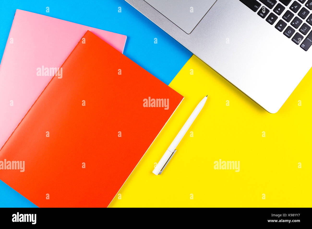 Top view of laptop computer, paper notebooks and white pen on blue and yellow color background