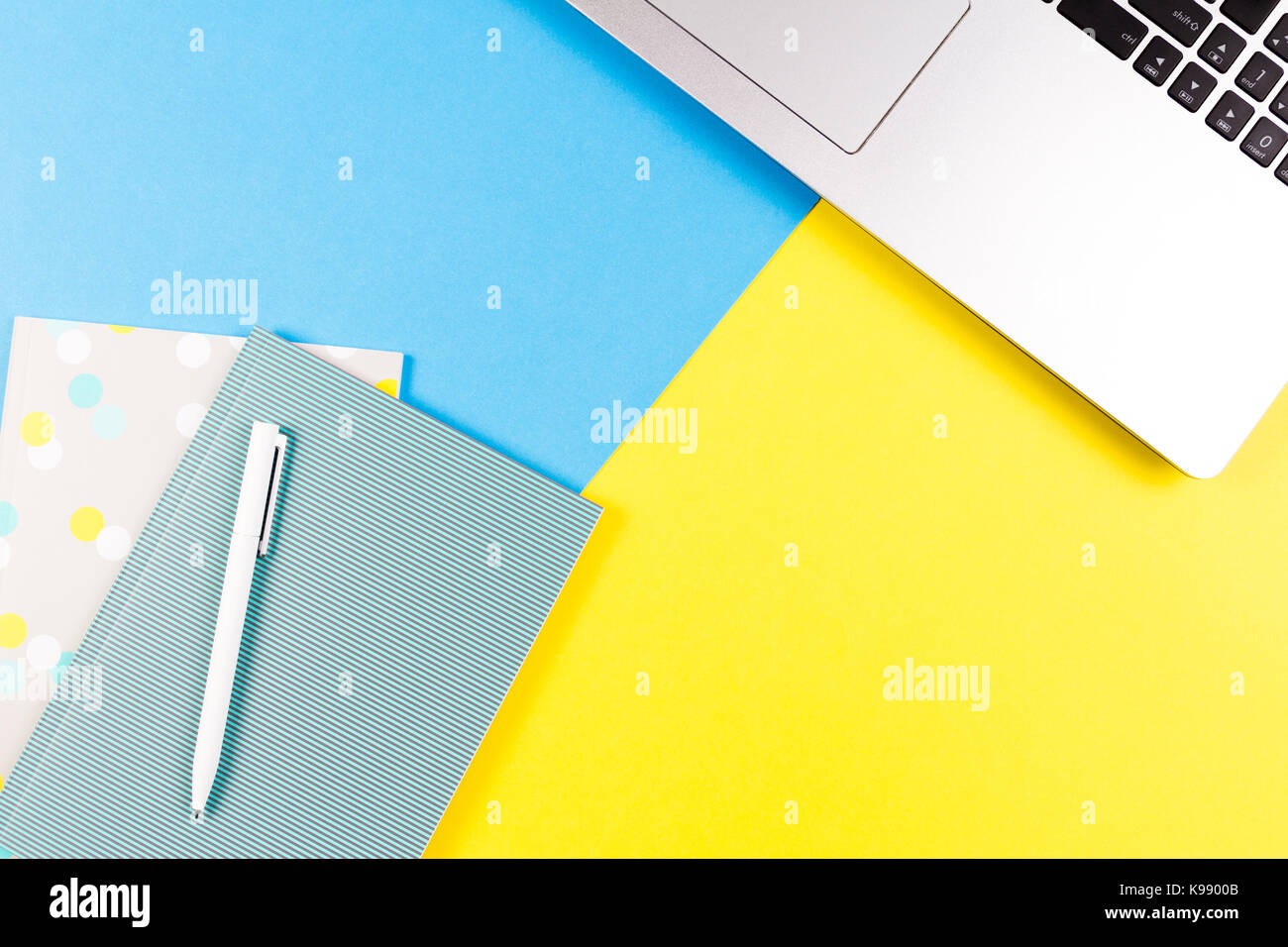 Top view of laptop computer, paper notebooks and white pen on blue and