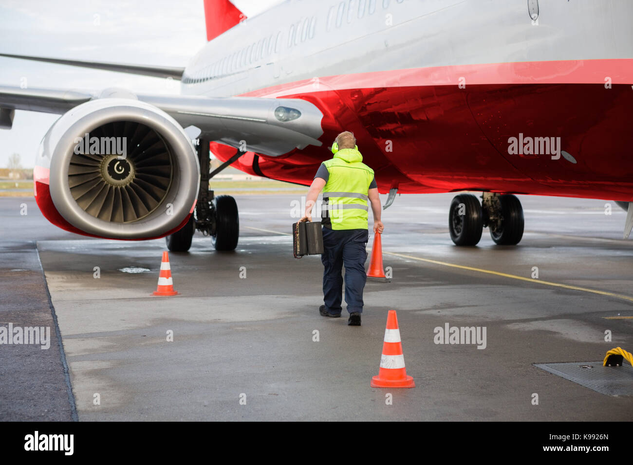Worker Carrying Traffic Cone And Chocks By Airplane On Runway Stock