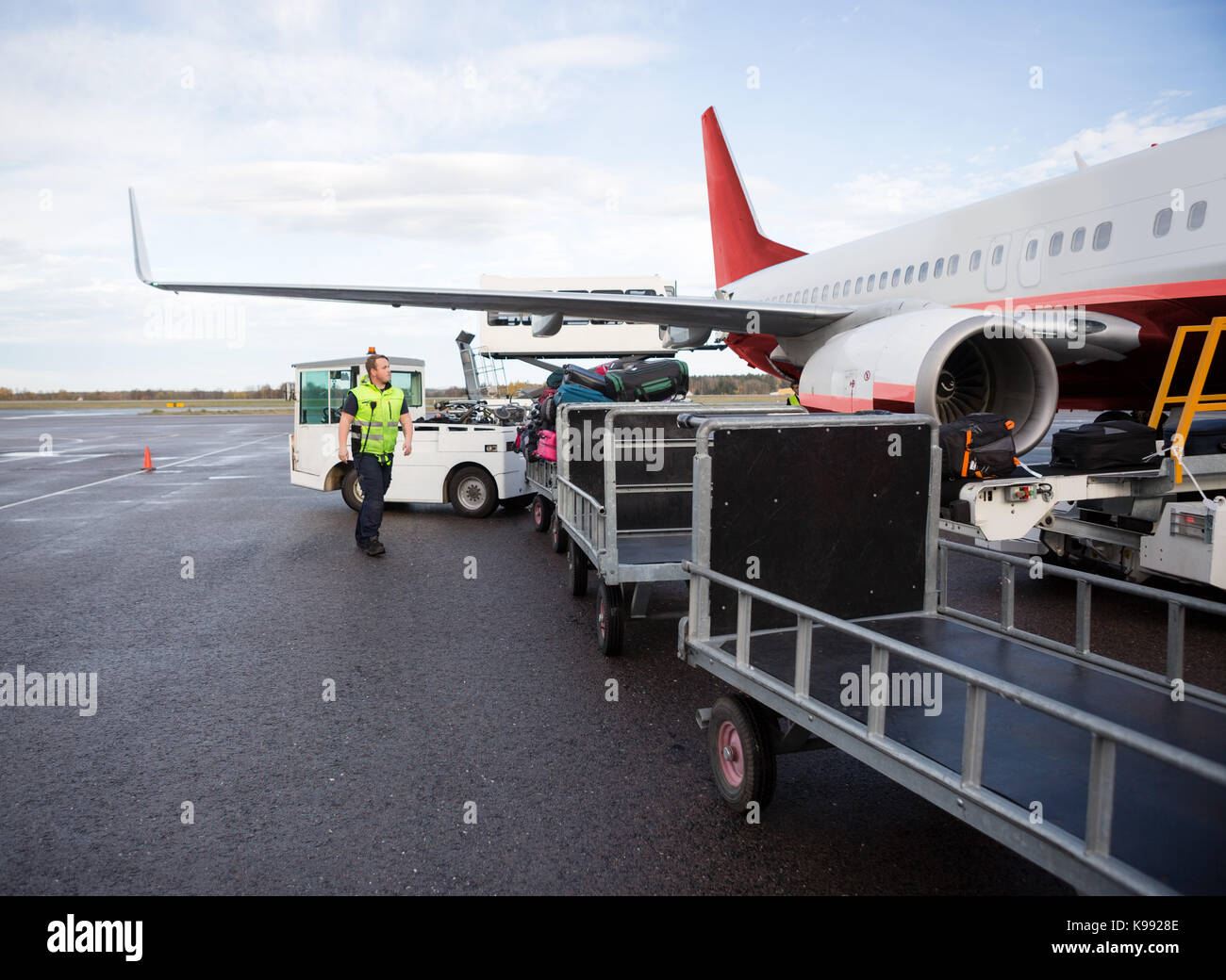 Worker Walking By Luggage Trailers On Runway Stock Photo