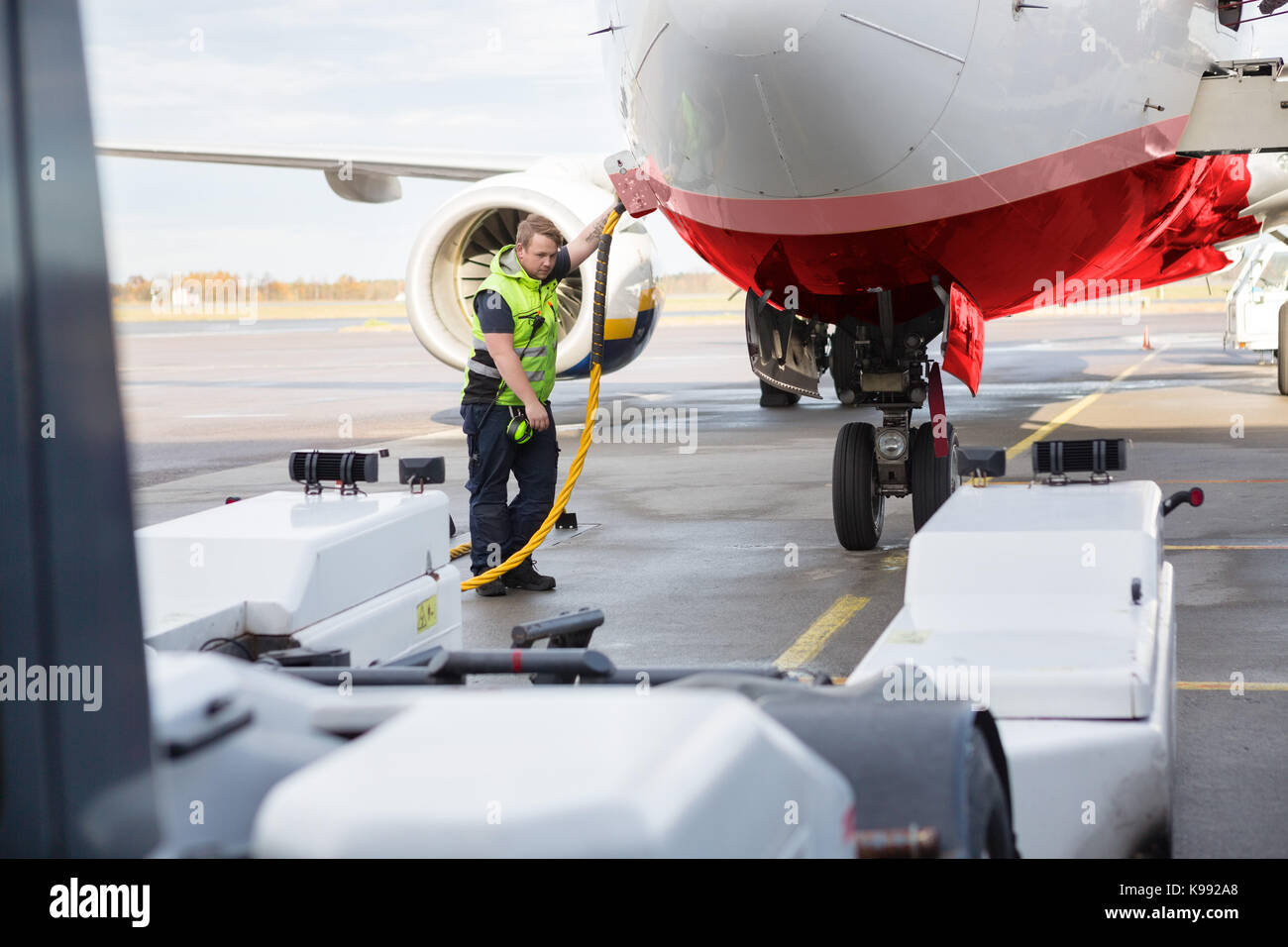 Mid Adult Crew Member Charging Airplane On Runway Stock Photo