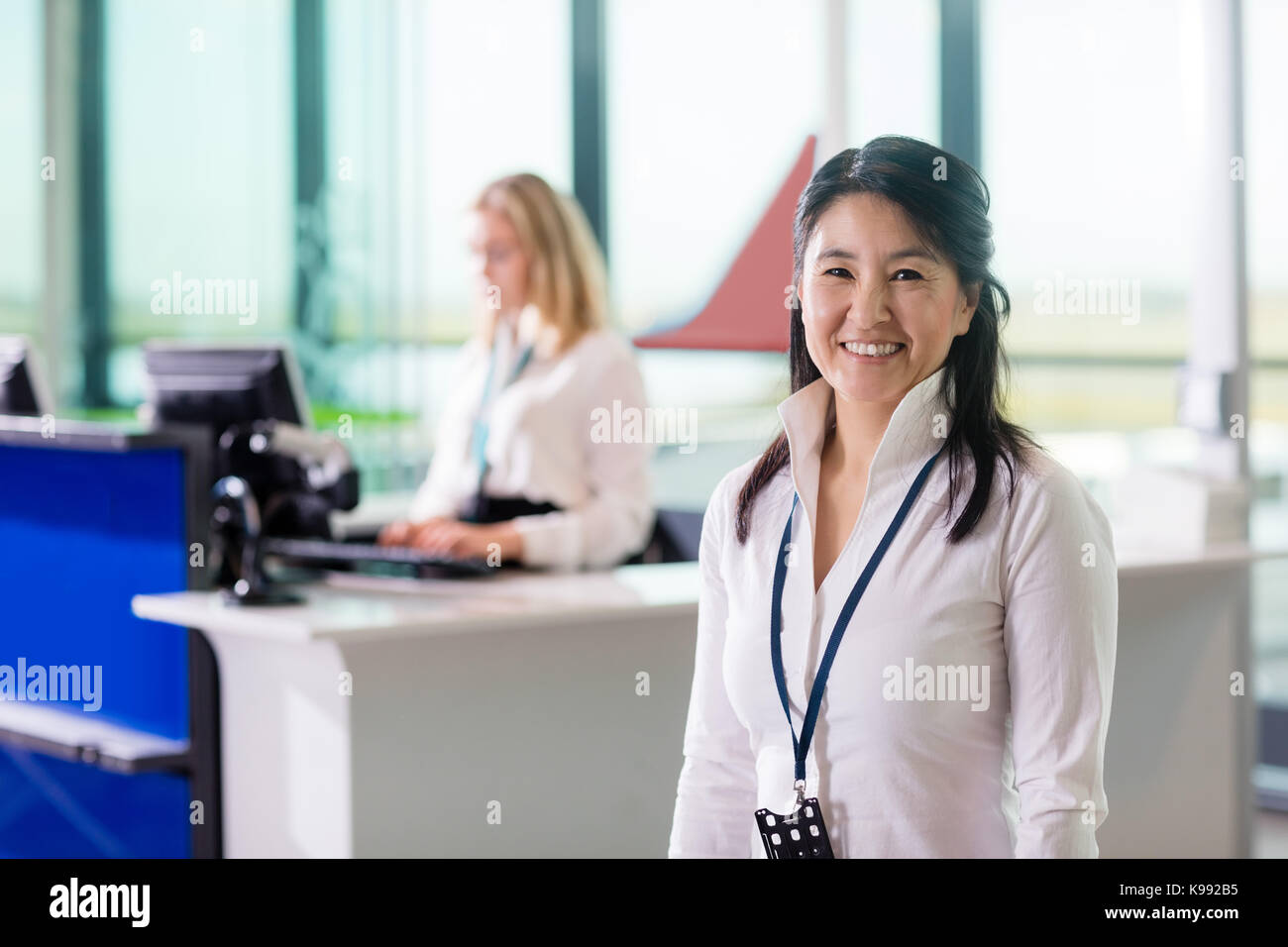 Ground Staff Smiling While Colleague Working At Airport Receptio Stock Photo