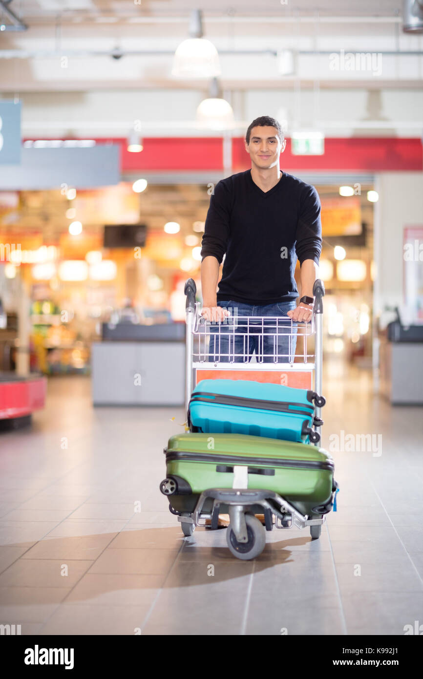 Handsome Young Man With Luggage In Cart At Airport Stock Photo