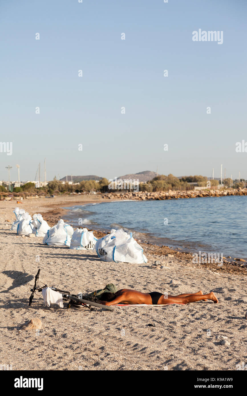A man is sunbathing in the beach of Glyfada (Athens, Greece) which is polluted by an oil spill. The white bags next to the man are full of crude oil. Stock Photo
