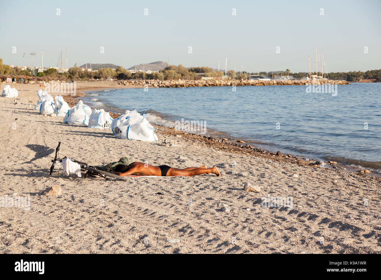 A man is sunbathing in the beach of Glyfada (Athens, Greece) which is polluted by an oil spill. The white bags next to the man are full of crude oil. Stock Photo