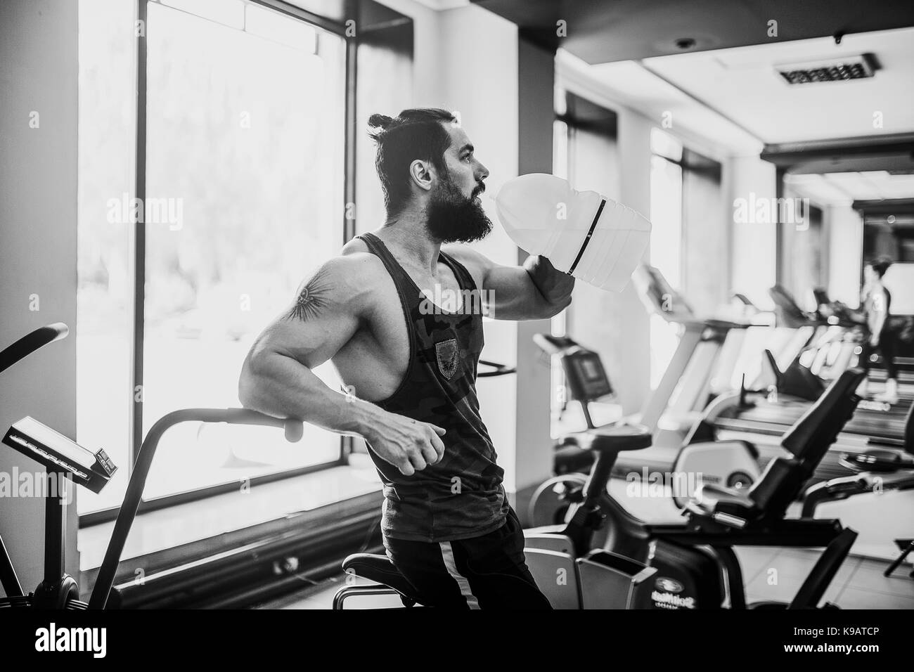guy relaxing after workout and hold or drink water from big bottle in