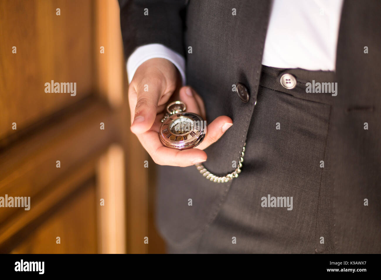 Man waiting for you. Dressing in black blazer, gray pants, brown leather  shoes, African American businessman sitting on railing in vintage style  office, looking at his wristwatch. Time is money.. Stock Photo