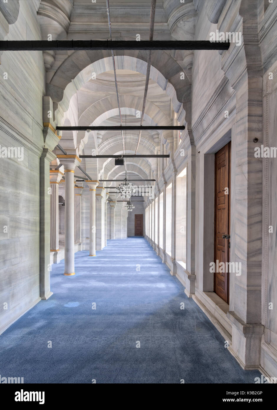 Passage in Nuruosmaniye Mosque, a public Ottoman Baroque style mosque, with columns, arches and floor covered with blue carpet lighted by side windows Stock Photo