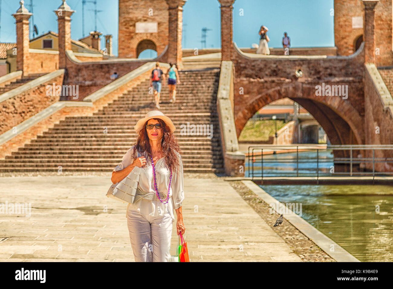 classy mature woman with wide hat and sunglasses near walking along water channel in lagoon town  in Italy Stock Photo