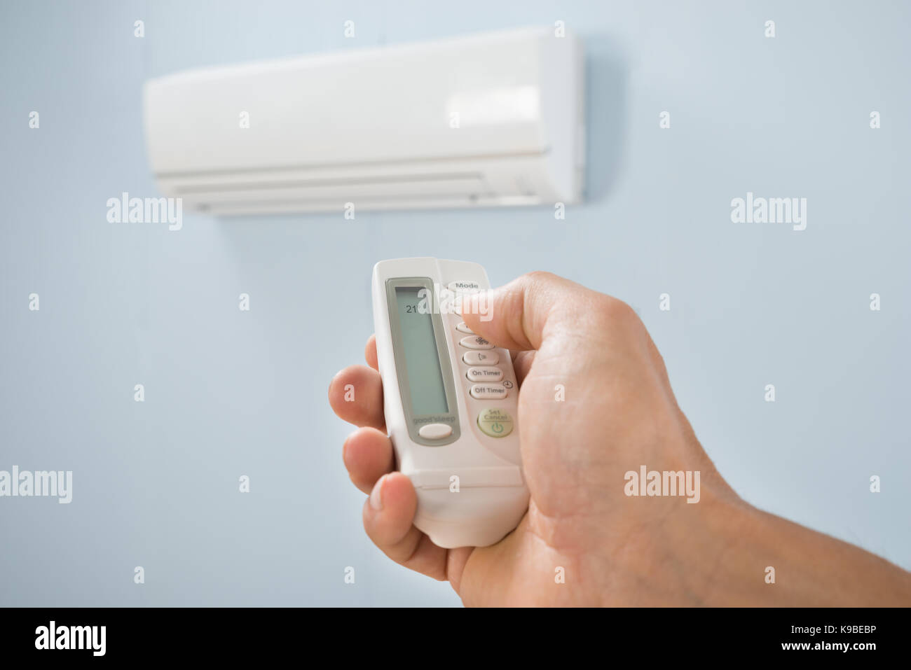 Man Adjusting Temperature Of Air Conditioner Using Remote Stock Photo
