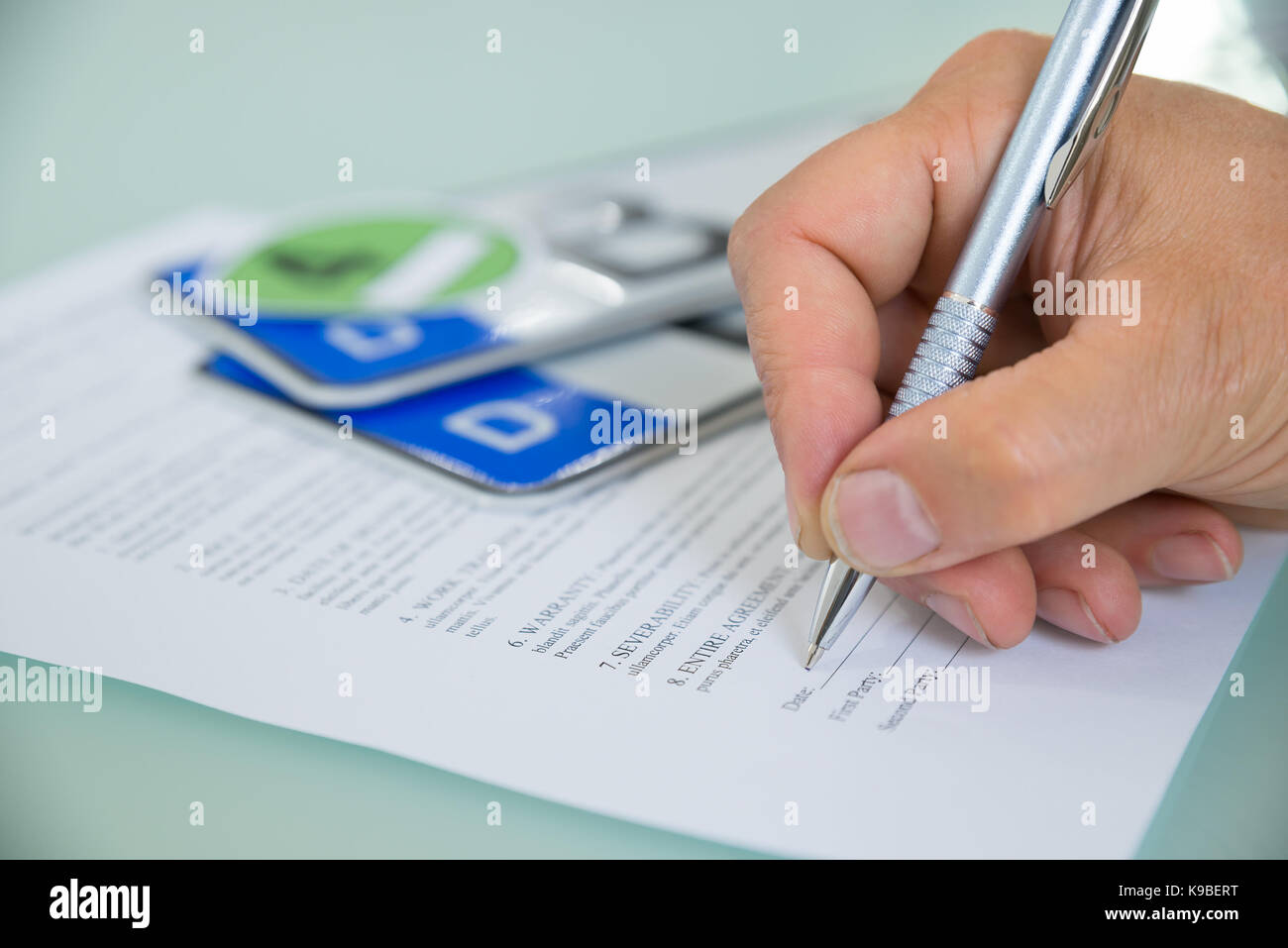 Close-up Of A Hand Filling Car Sale Contract Form With Vehicle Registration Plate On Desk. Contract Paper Contains Placeholder Text Stock Photo