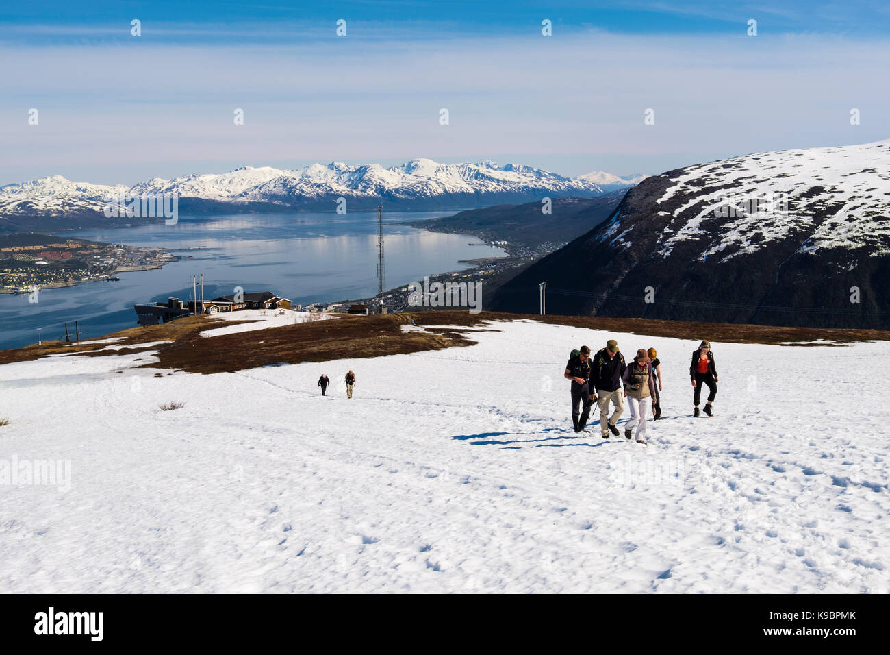 Hikers walking through snow from Fjellheisen Cable Car top station on Mount Storsteinen in summer. Tromso, Troms, Norway, Scandinavia Stock Photo
